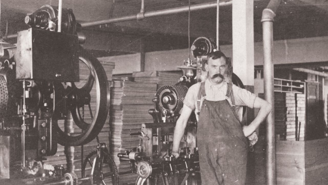 Man standing next to playing card machine in early 1900s, Factory 25